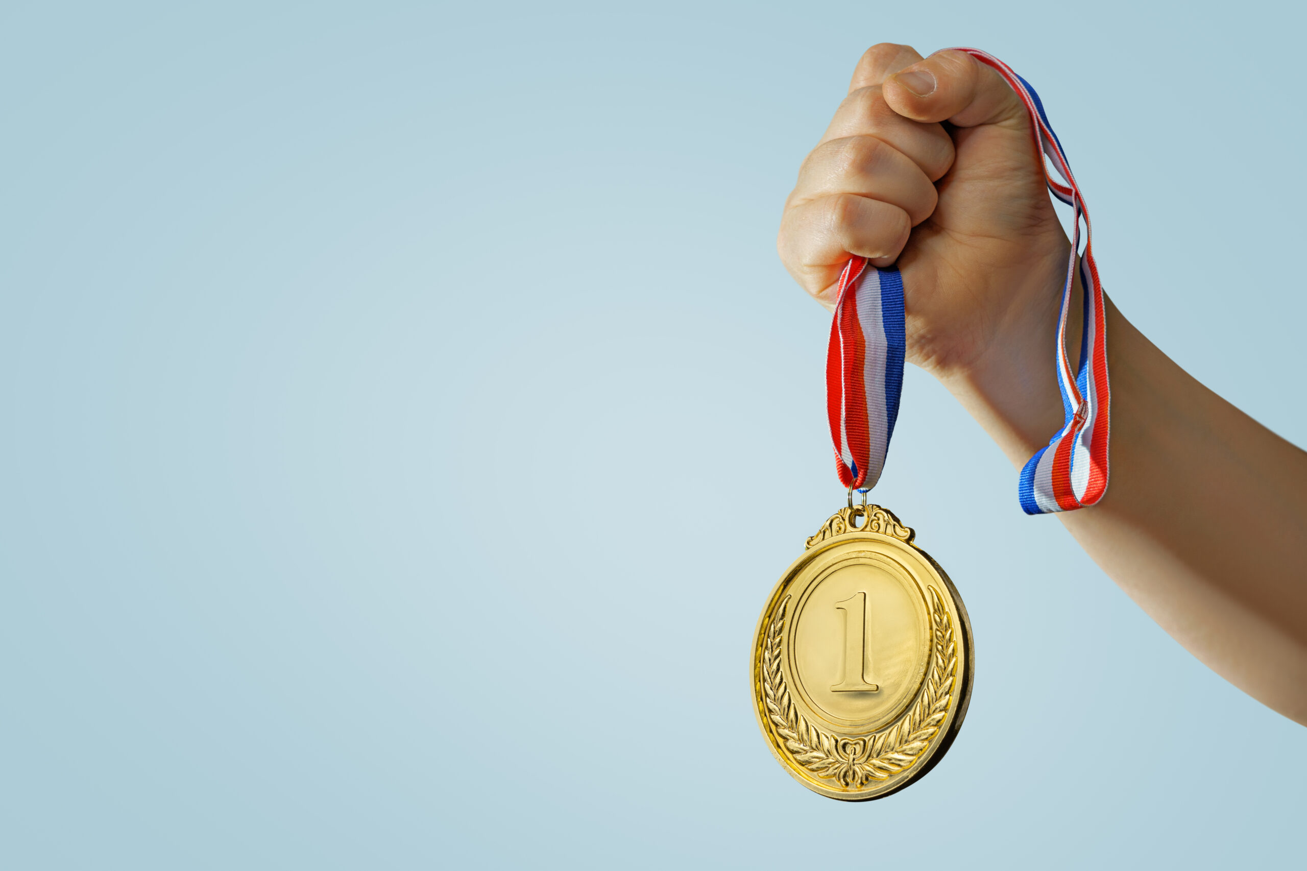 Eine Kinderhand hält eine Medaille für den ersten Platz hoch.