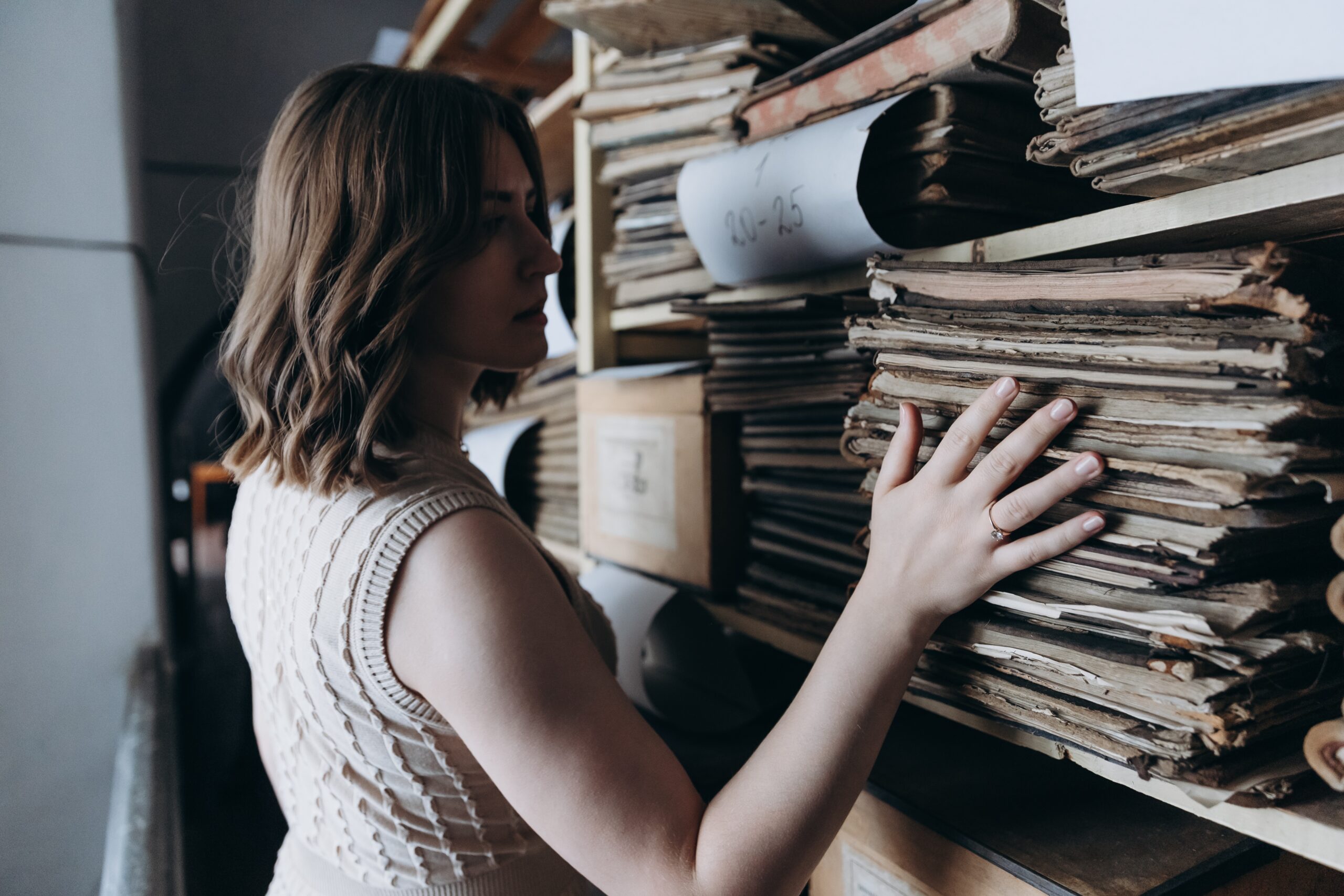 Eine Frau steht vor einem großen Regal mit vielen alten Büchern.