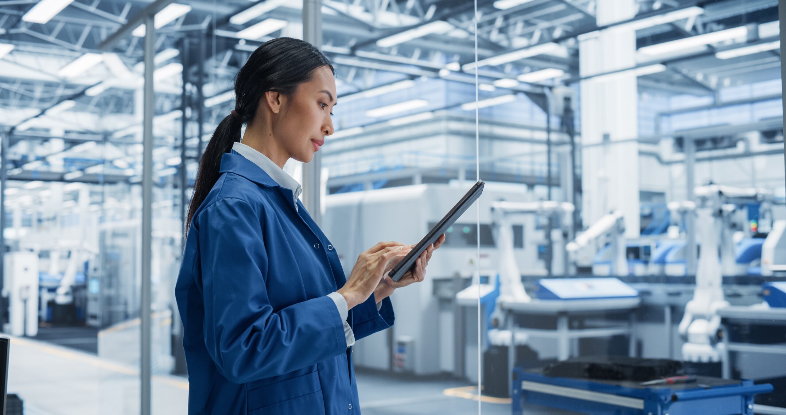 Eine Ärztin steht in einem modernen Labor mit Robotern und schaut auf ihr Tablet in ihren Händen.