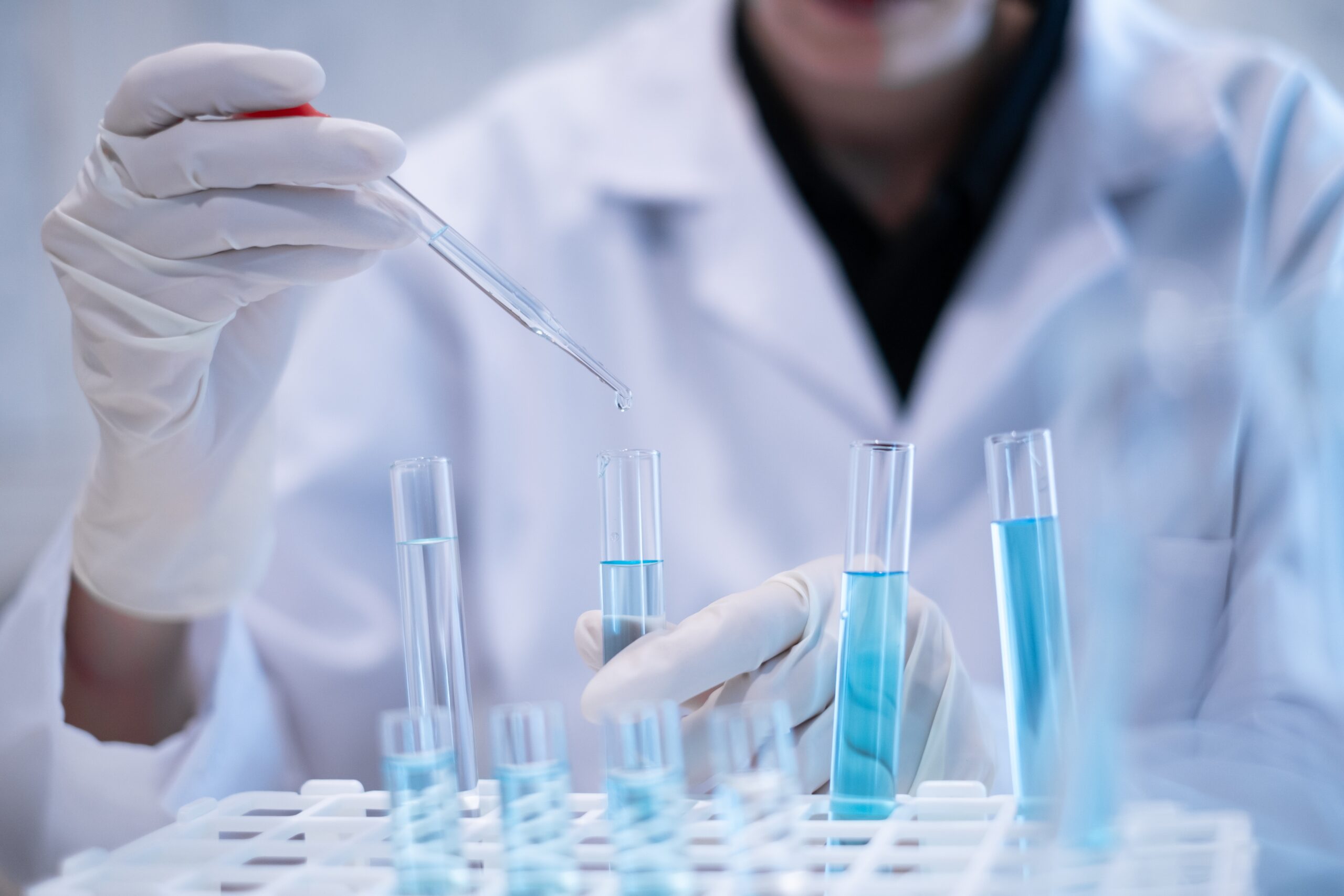 Ein Wissenschaftler pipettiert eine blaue Flüssigkeit in Reagenzgläser.